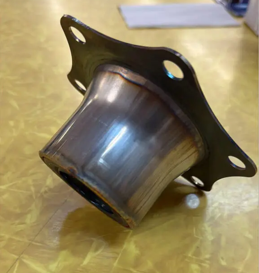 A Torque Tube Seal Plate with a cylindrical center and four bolt holes sits on a yellow textured surface.