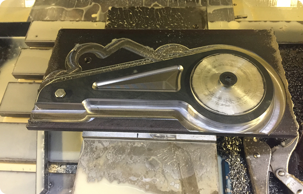 A metal part is being machined on a CNC milling machine, with visible cutting marks and metal shavings surrounding the workpiece.