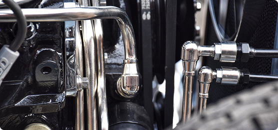 Close-up view of polished metal pipes and connectors in a car engine compartment, showing detailed automotive components and mechanical parts.